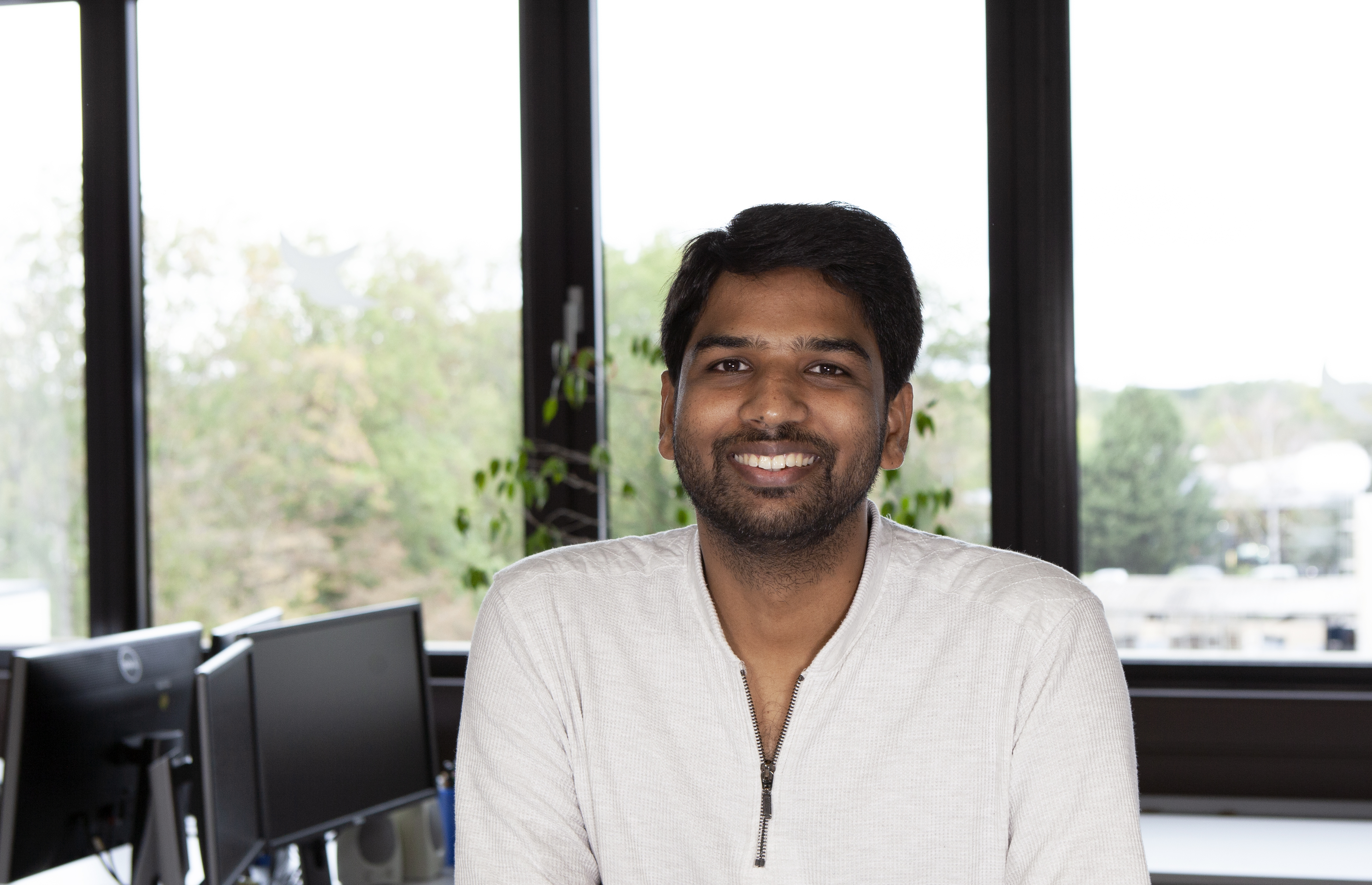 Doktorand lächelt in die Kamera vor einem Bürohintergrund.