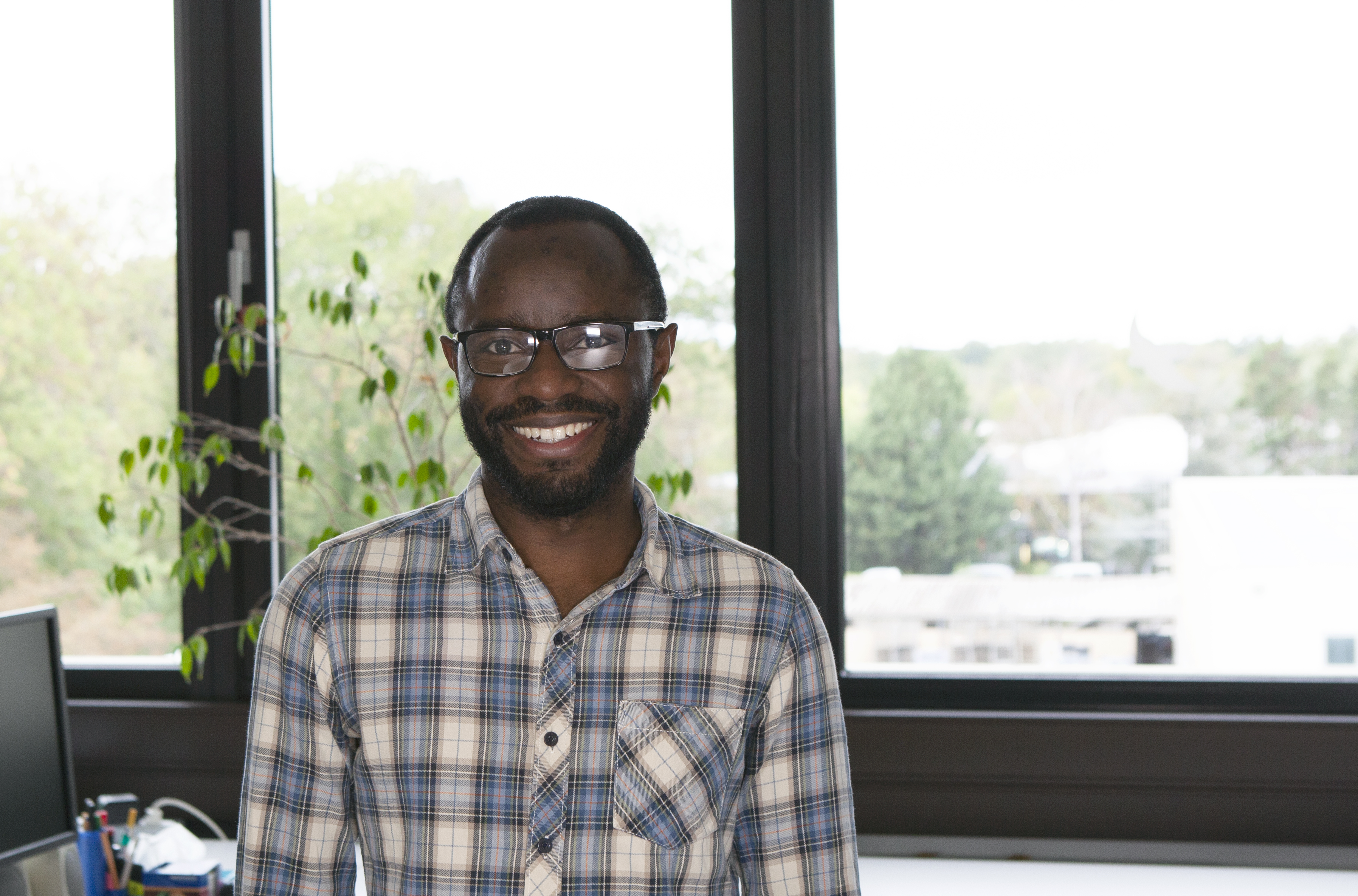 Doktorand lächelt in die Kamera vor einem Bürohintergrund.