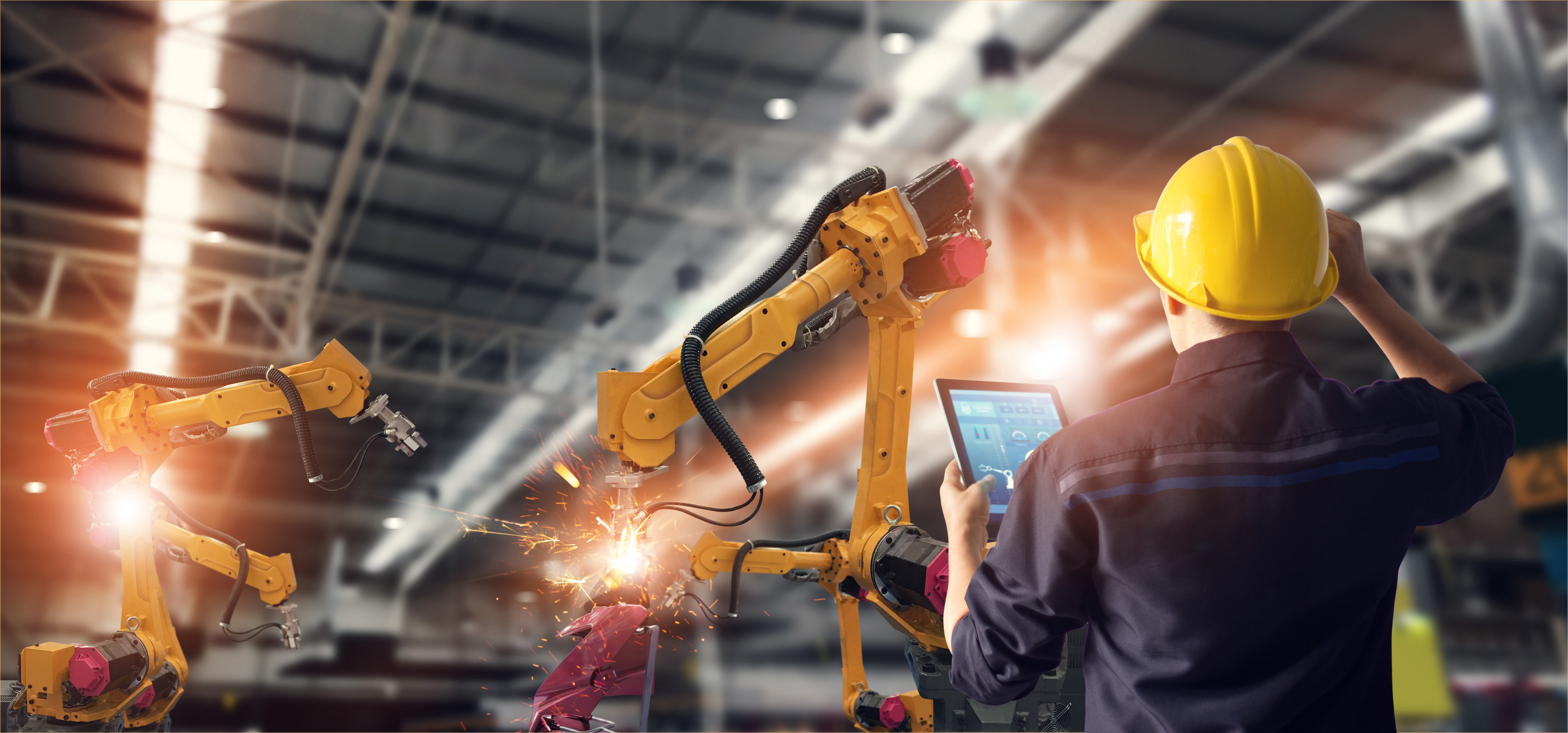 automatisierte Fertigungsanlage mit orangenen Roboterarmen und einem Arbeiter