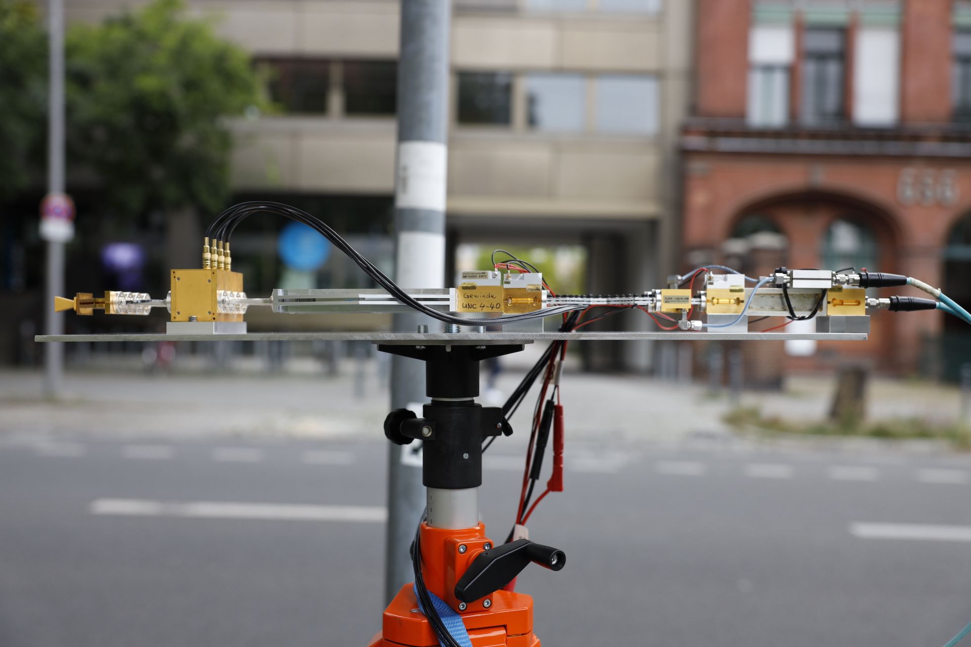 Hochfrequenzkomponenten sind zu einem Messaufbau verbunden, im Hintergrund sieht man leicht verschwommen zwei Gebäude und eine Verkehrsstraße.