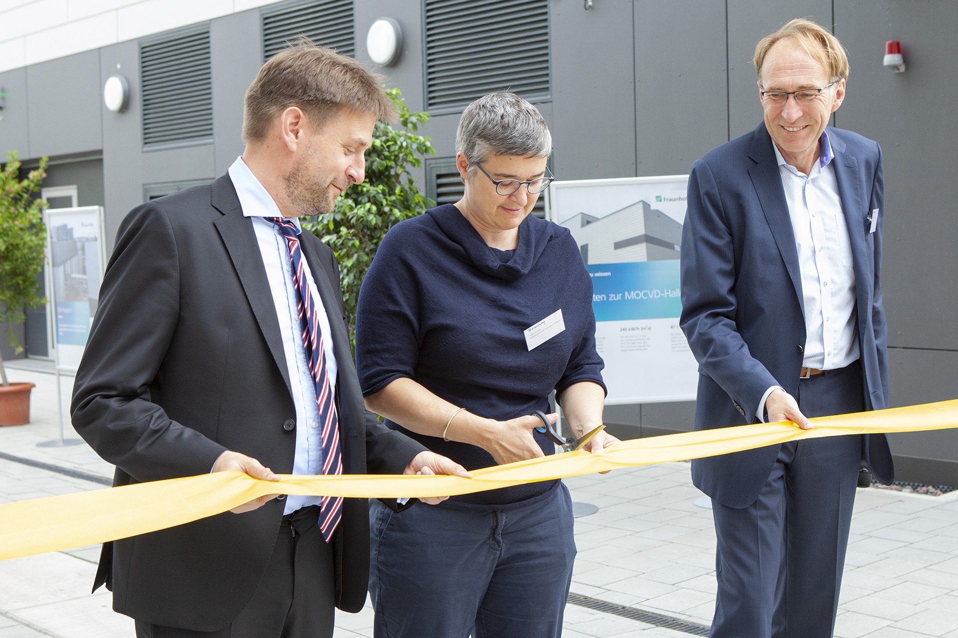 Two men and a woman ceremoniously cut a golden ribbon at the building inauguration of the new buildings at Fraunhofer IAF.